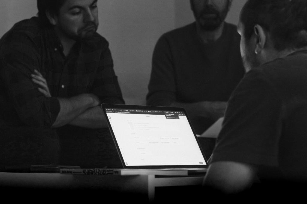 Black and white photo of three people in a meeting, gathered around a laptop displaying search results on a screen.