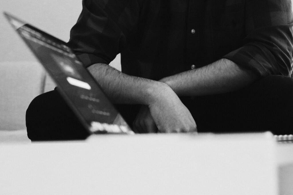 Black and white photo of a person sitting with folded arms beside an open laptop, representing a discussion about building backlinks, and how they are still important for SEO.