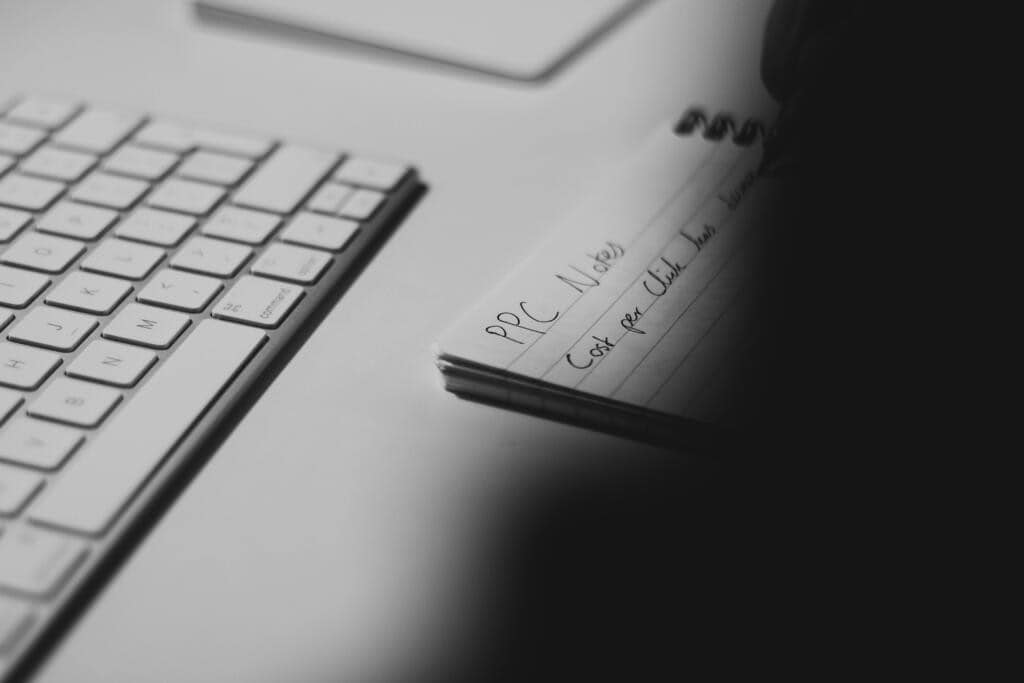 Black and white photo of a desk with a keyboard and a notepad titled ‘PPC Notes,’ showing someone writing about the meta andromeda update
