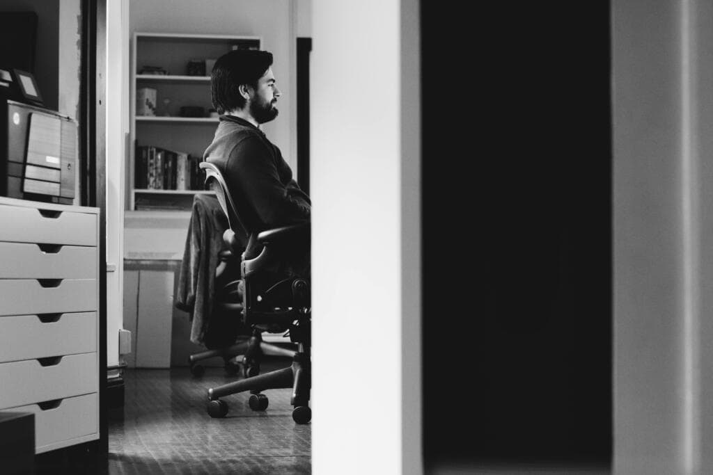Black and white photo of a man seated at a desk in an office searching for information through AI-powered tools alongside traditional search engines.